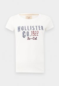 Hvit bomulls T-skjorte med rund hals og korte ermer. Framsiden viser blå og rød trykt tekst: "HOLLISTER CO. 1922 So-Cal."