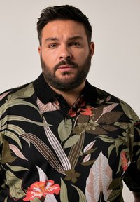 Pletené triko s květinovým vzorem, které má černý základ s barevnými listy a květinami, klasický límec a zapínání na tři knoflíky.
