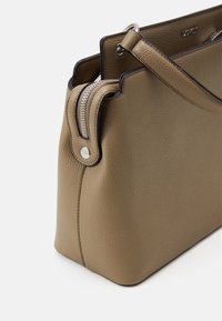 Sac tote en cuir marron avec une surface texturée, fermeture zippée et une bandoulière amovible. Conçu avec des finitions en métal argenté et des bords noirs contrastants.