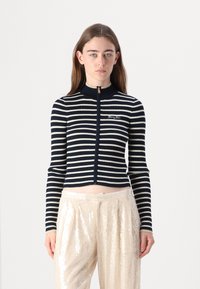 Navy and cream striped ribbed zip-up cardigan with a high collar and gold zipper, paired with light sequined wide-leg pants.