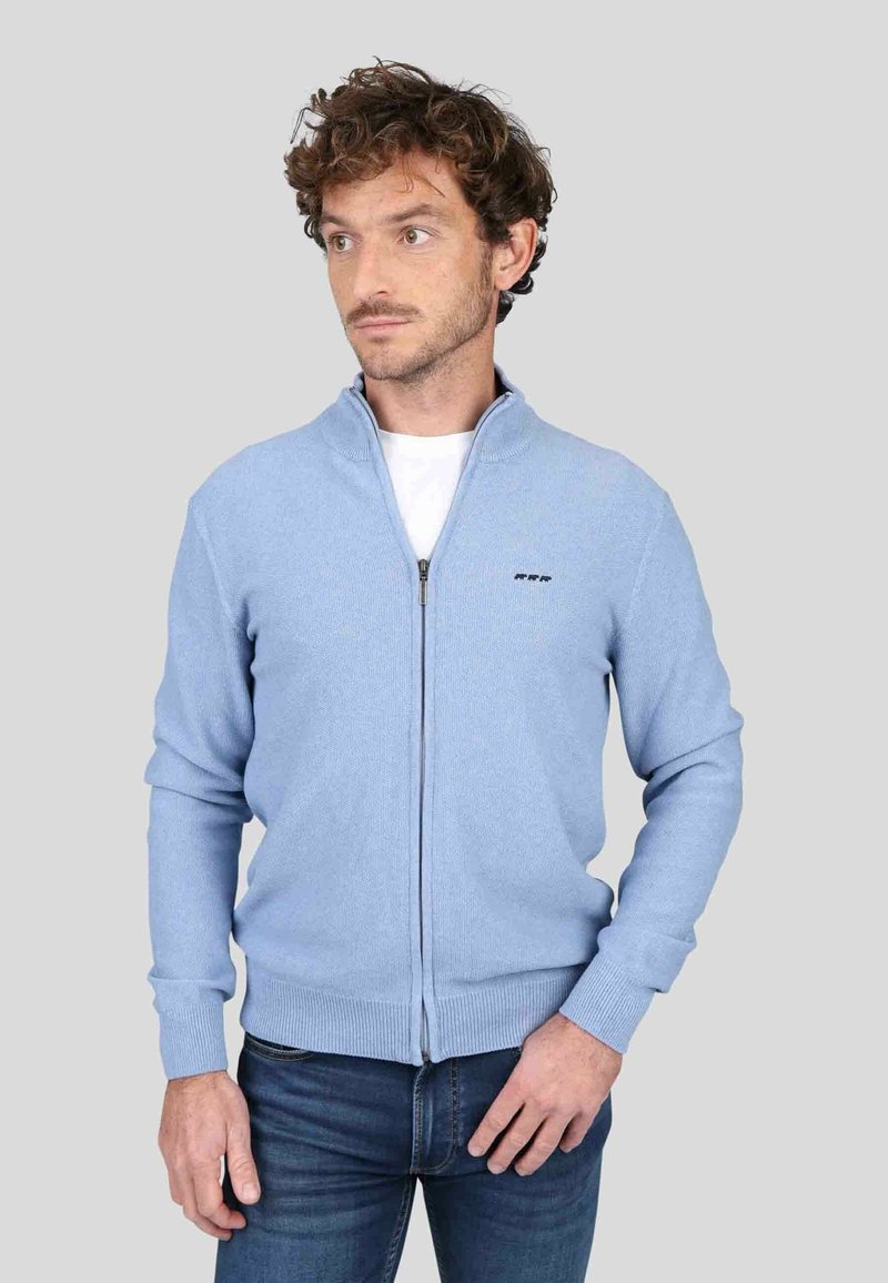 Cardigan zippé bleu clair avec col haut, bords côtelés et un motif tricoté texturé. Détail du logo simple sur la poitrine.