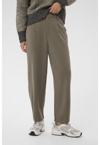 Pantaloni verde oliva con una vestibilità rilassata, davanti plissettato e tasche laterali, abbinati a scarpe sportive grigio chiaro con dettagli in rete e gomma.