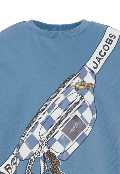 T-shirt en coton bleu avec un motif graphique représentant un sac à carreaux avec un taxi jaune, un détail de fermeture éclair et l'étiquette « JACOBS » en typographie audacieuse.