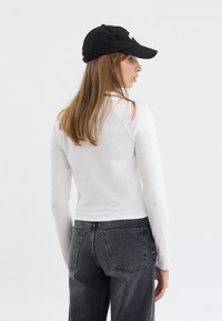 Hvit langermet topp kombinert med mørk grå denim jeans. Personen har på seg en svart caps, noe som gir en avslappet, tettsittende silhuett.