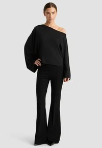 Schwarzes Off-Shoulder-Oberteil mit langen Ärmeln, kombiniert mit schwarzen Schlaghosen. Glatte Textur, minimalistisches Design und uniforme Farbe.