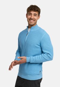 Helles blaues Strickpullover mit einem Reißverschlusskragen, gerippten Bündchen und Saum. Verfügt über ein strukturiertes Muster und ein kleines Logo nahe dem Saum.