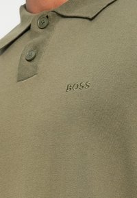 Olijfgroene polo shirt van gestructureerde brei stof, met een twee-knopen placket en een reliëf "BOSS" logo op de borst.