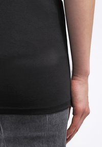 Černé bavlněné tričko, slim fit design, krátké rukávy a zaoblený lem. Měkká textura s hladkým povrchem, nošeno s šedými džíny.