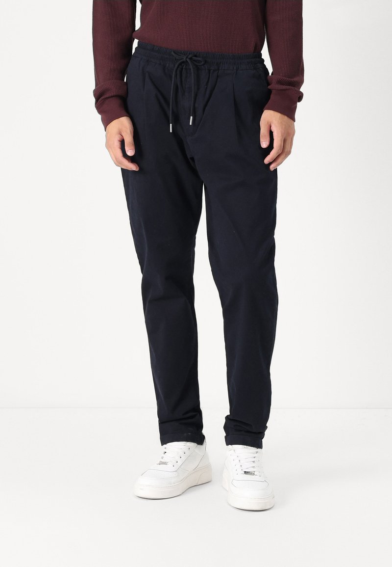 Marineblå bomullsblandings joggebukser med elastisk midje, justerbar snor og side lommer, kombinert med hvite sneakers.