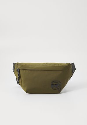 Saco de cintura de tecido verde-oliva com uma textura suave, apresentando um detalhe de logotipo preto e acabamentos de alças listadas em preto e branco.