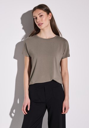 Khaki short-sleeve t-shirt made of soft fabric, round neckline, relaxed fit, paired with black pants, with visible pockets.