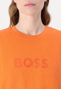 Orange cotton t-shirt with a round neckline, featuring a tonal "BOSS" logo printed on the front in a slightly darker shade of orange.