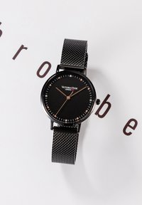 Czarny zegarek na siateczkowym pasku z okrągłą czarną tarczą, różowozłotymi znacznikami godzin i wskazówkami. Posiada minimalistyczny design z logo na dole.