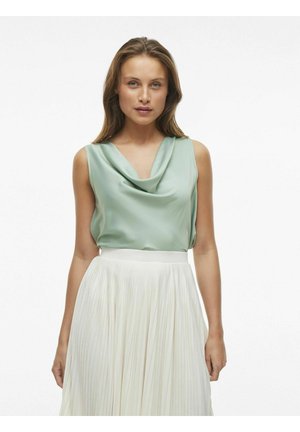 Top de satén color verde claro con cuello de capa, combinado con una falda plisada color crema. Textura suave y silueta fluida, adecuada para ocasiones formales.