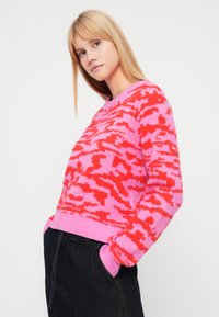 Pink and red patterned sweater with a crew neckline, ribbed cuffs, and hem. Crafted from a soft, knit material, featuring a relaxed fit.