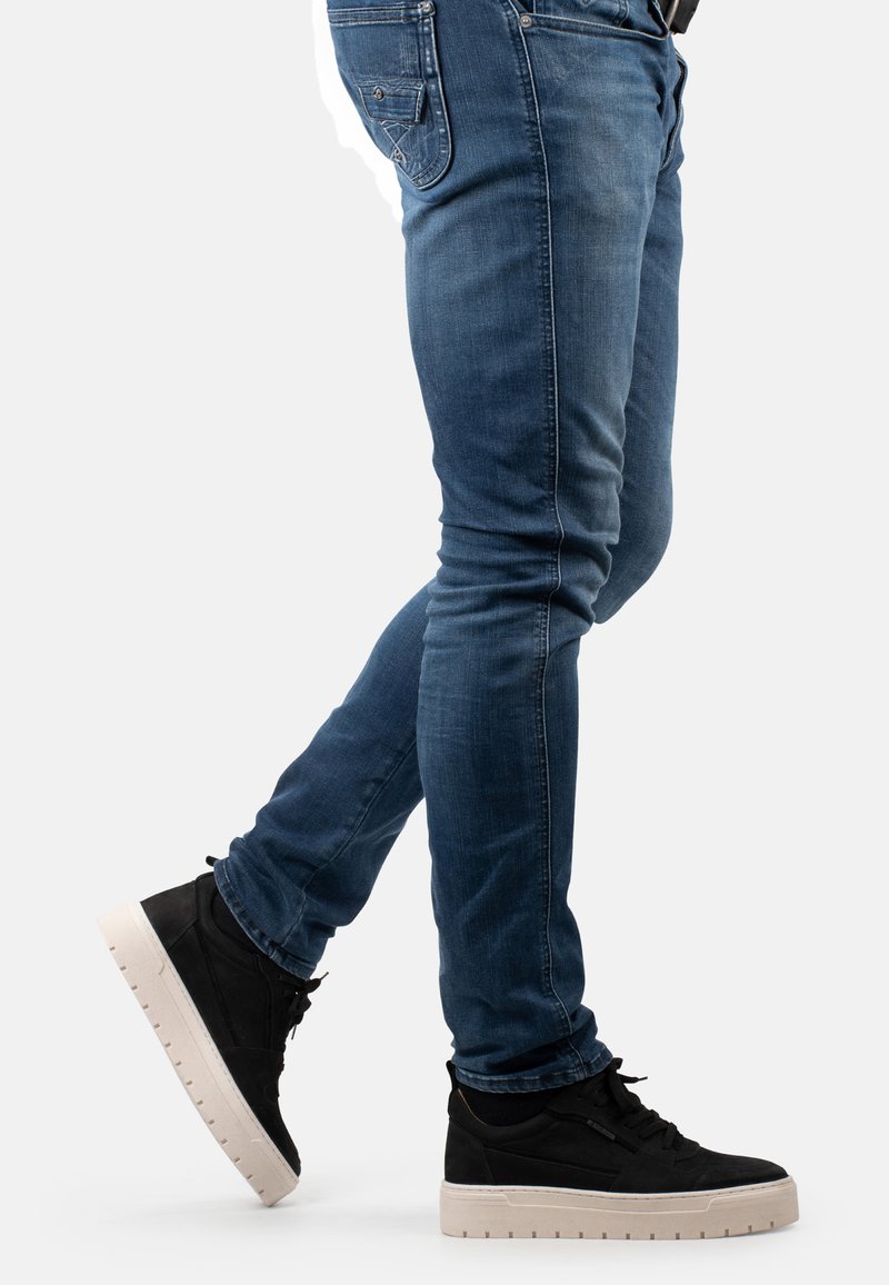 Jeans skinny in denim blu con un lavaggio sbiadito, e sneakers alte nere con suole bianche, dotate di asole e lacci.