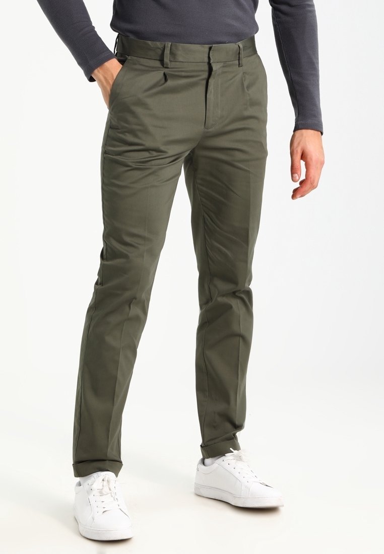 Pantaloni verde oliva realizzati in tessuto liscio, con una vestibilità sartoriale, tasche anteriori e una vita classica. Abbinati a sneakers bianche.
