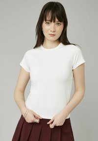 T-shirt blanc à manches courtes avec un col rond, en tissu doux, présentant une coupe ajustée et une surface légèrement texturée.