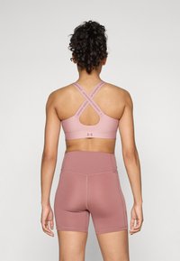 Sujetador deportivo rosa con tirantes cruzados y diseño de ojal, combinado con pantalones cortos de talle alto a juego, ambos presentan una tela suave y costuras mínimas.
