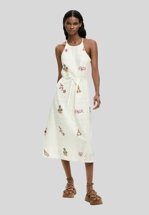 Nő fehér, ujjatlan, középhosszú ruha, virág- és madárhímzéssel, deréknál megkötve, barna platform szandállal párosítva.