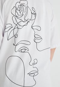 Bílý tričko s černými liniemi znázorňujícími dva abstraktní obličeje a růži, s hladkými, souvislými obrysy a minimalistickým designem.