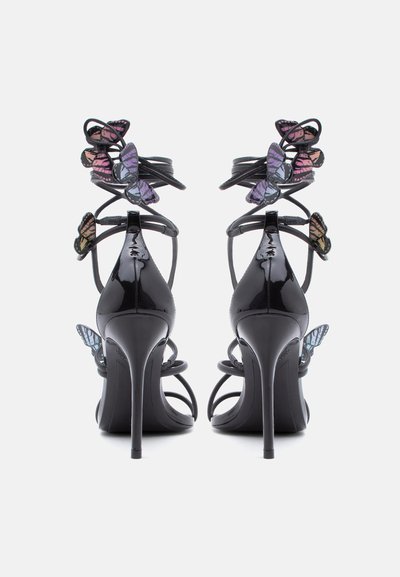Μαύρα σανδάλια με ψηλό τακούνι και σπιράλ λουριά στον αστράγαλο, στολισμένα με πολύχρωμες πεταλούδες, φωτογραφημένα από πίσω σε λευκό φόντο.