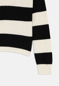Stickad tröja med svarta och krämfärgade horisontella ränder, rund halsringning, ribbade muddar och fåll. Slät textur, mjukt material.