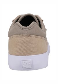Béžové plátěné tenisky s texturovaným svrškem, gumovou podrážkou a bílou protišmykovou podešví. Vyznačují se logem DC na patě a minimálními detaily šití.