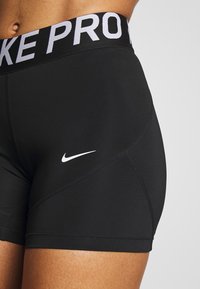 Primo piano di una persona che indossa pantaloncini sportivi neri Nike Pro con il logo swoosh bianco e la scritta "NIKE PRO" sulla cintura.