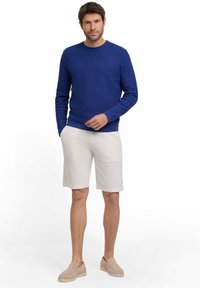 Blauer strukturierter Pullover, weiße gewobene Shorts und helle, bequeme Slipper. Alle Teile zeichnen sich durch eine lässige, lockere Passform und ein unkompliziertes Design aus.