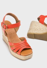 Sandales compensées en cuir rouge avec une plateforme recouverte de jute, présentant plusieurs brides et un accent de boucle métallique. Doublure intérieure marron.