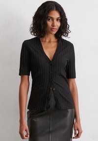 Schwarze, gerippte Kurzarm-Cardigan mit V-Ausschnitt, ausgestattet mit einer Reihe schwarzer Knöpfe auf der Vorderseite. Glatte Textur, lockere Passform.