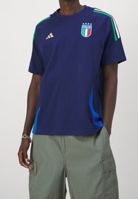 Granatowa bawełniana koszulka sportowa z logo Włoch i trzema gwiazdami, z zielonymi, białymi i czerwonymi paskami akcentującymi na ramionach oraz niebieskimi panelami bocznymi.