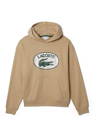 Sudadera beige con capucha, bolsillo tipo canguro delantero y logo verde de Lacoste con un cocodrilo dentro de un óvalo en el pecho.