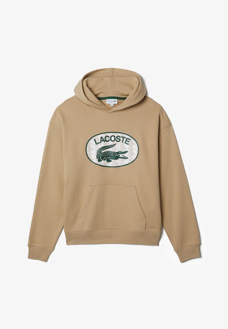 Sweat à capuche beige avec poche kangourou à l’avant et logo Lacoste vert représentant un crocodile à l’intérieur d’un ovale sur la poitrine.