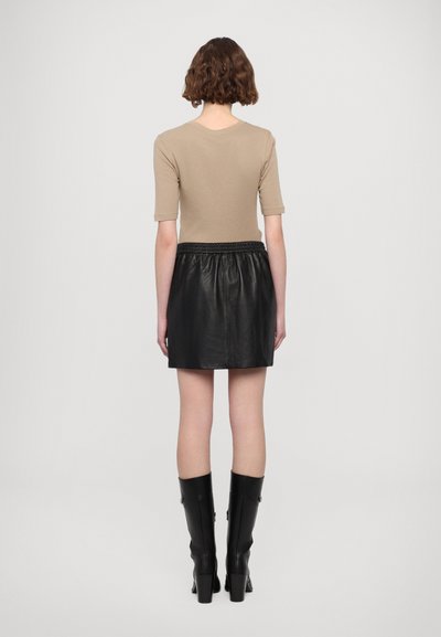 Beige fitted top with short sleeves, paired with a black leather mini skirt featuring an elastic waistband. Model wears black knee-high boots.