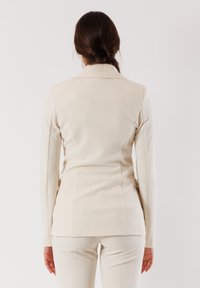 Blazer bianco su misura con una silhouette aderente, colletto a scello e maniche lunghe, caratterizzato da una texture liscia e un design elegante.