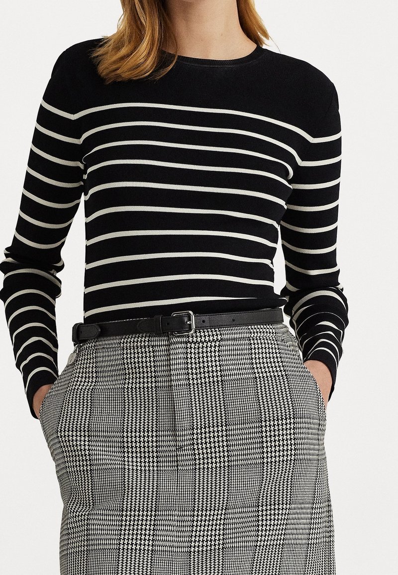 Femme portant un haut à manches longues rayé noir et blanc horizontalement et une jupe à carreaux noir et blanc taille haute avec les mains dans les poches.