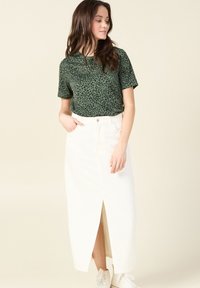 Camiseta de manga corta con estampado de leopardo verde combinada con una falda maxi de mezclilla blanca con abertura frontal y bolsillos, estilizada con zapatillas blancas.