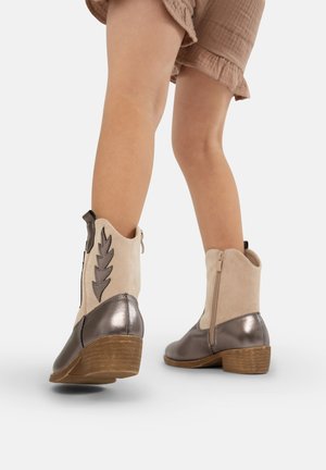 Tans en zilveren enkelboots met een ritssluiting, voorzien van een tekstuur suede bovenkant en een metalen hak. Bladvormig patroondetail aan de zijkant. Houtachtige hak.