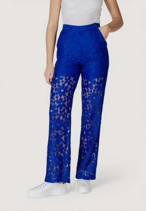 Pantaloni blu in pizzo con un motivo floreale, gambe inferiori trasparenti, silhouette a gamba larga e vita alta, abbinati a sneakers bianche.