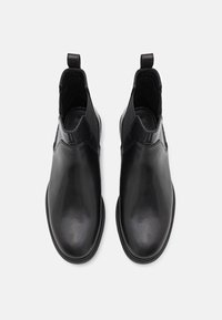 Černé kožené kotníkové boty s elastickými postranními panely, kulatou špičkou, poutky na zadní straně a texturovanou podrážkou pro lepší přilnavost.