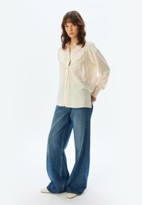 Crème knoopshirt met bloemenborduurwerk, gecombineerd met wijde blauwe denim jeans, met een relaxed fit en zachte textuur.
