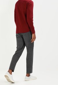 Camicia a maniche lunghe a scacchi rossi, pantaloni grigi texturizzati e sneakers bianche. I pantaloni hanno un taglio affusolato con una leggera apertura alla caviglia.