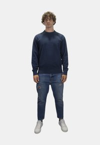 Felpa marina in cotone, abbinata a jeans blu con effetto logoro e sneakers bianche; presenta un collo a giro e polsini a costine.