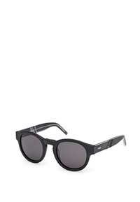 Gafas de sol redondas y negras con un acabado mate y lentes oscuros. Presentan puntas de patillas de acetato transparente con sutiles acentos a rayas.
