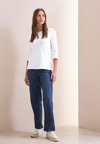 Bílý dlouhý rukáv, volný střih; kombinovaný s modrými rovnými džíny a bílými teniskami. Hladká tkanina, jednoduchý design, minimální detaily.