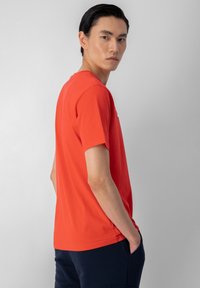 Camiseta de algodón roja con mangas cortas, cuello redondo y un corte holgado. Llevada con pantalones azul marino, mostrando un color sólido y suave.