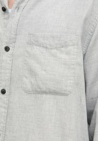 Lichtgrijs overhemdd blouse gemaakt van textiel, met een borstzak en zwarte knopen voor sluiting. Eenvoudig en casual ontwerp.