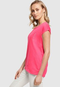 Fuksijos spalvos trumpas rankovė t–shirt, pagamintas iš minkštos medžiagos, su paprastu rožės grafiku. Marškiniai turi laisvą pjaustymą ir apvalų kaklą.